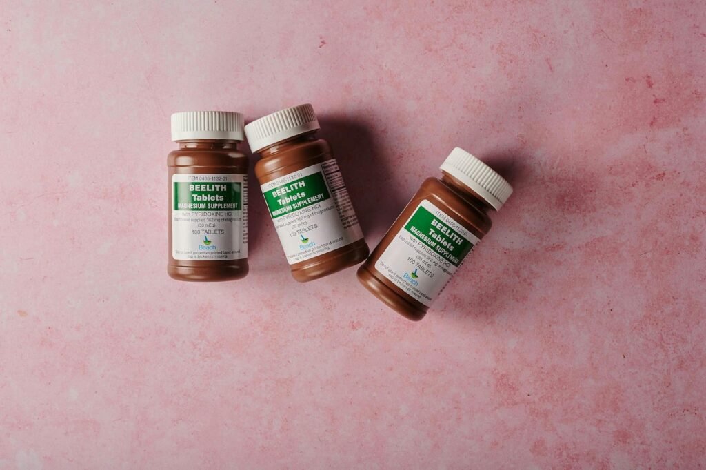 pexels-photo-17604755-17604755 Three brown bottles of magnesium tablets on a soft pink background, ideal for health-themed content.