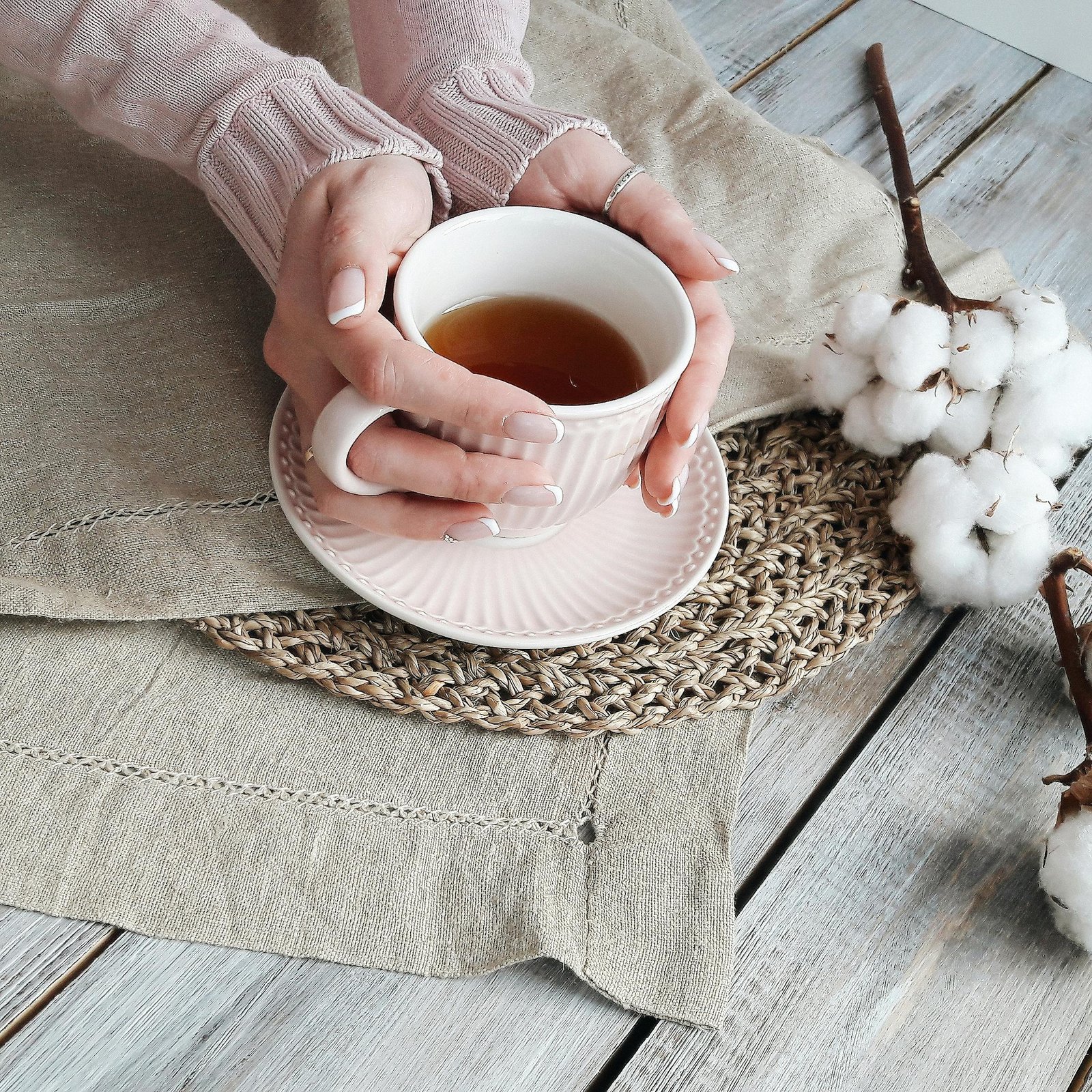 Hands holding a warm cup of tea surrounded by rustic textiles and cotton.